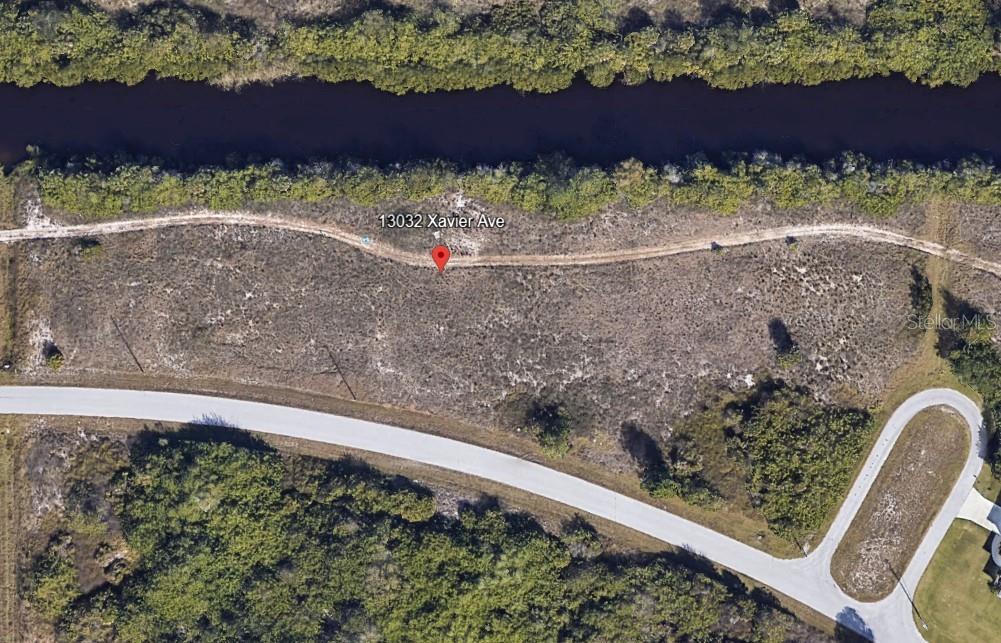 An aerial view shows a vacant, undeveloped lot bordered by a road and a canal — 13032 XAVIER AVENUE, PORT CHARLOTTE, FL
