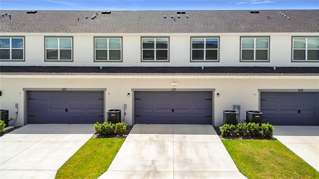 An exterior view of a multi-unit townhouse building with three garage doors and driveways — 371 CROSSINGS AVENUE, ST CLOUD, FL