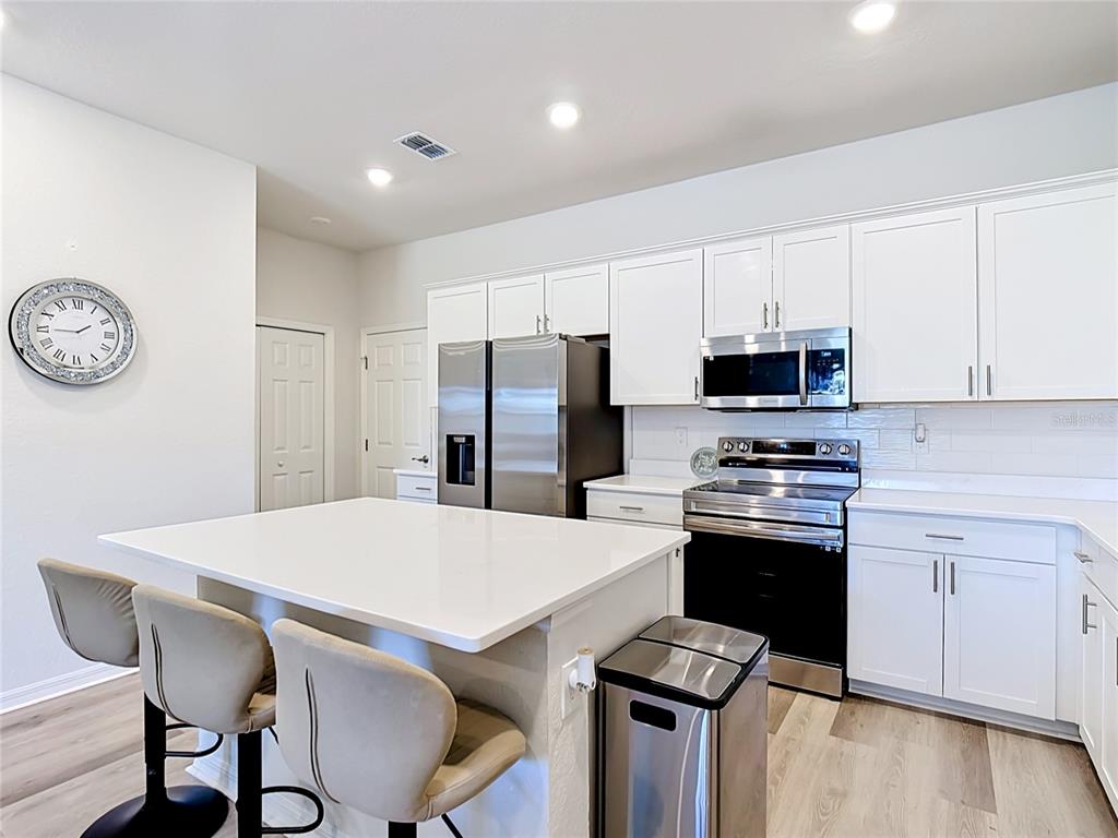 A modern kitchen features white cabinets, stainless steel appliances, a quartz island, and bar stools — 371 CROSSINGS AVENUE, ST CLOUD, FL