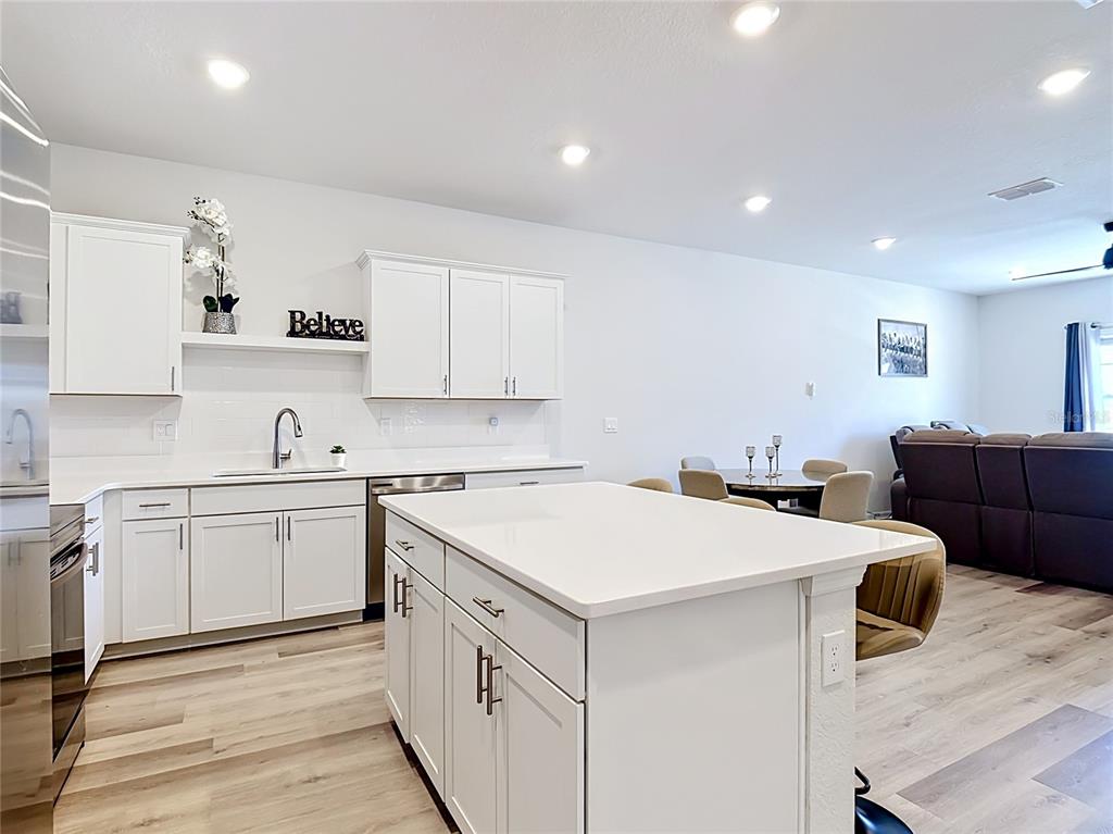 A white kitchen features a central island, quartz countertops, and light wood-look flooring — 371 CROSSINGS AVENUE, ST CLOUD, FL