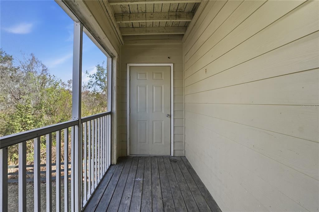 A screened-in wooden balcony features a beige door and horizontal siding on the exterior wall — 18311 BRIDLE CLUB DRIVE, TAMPA, FL