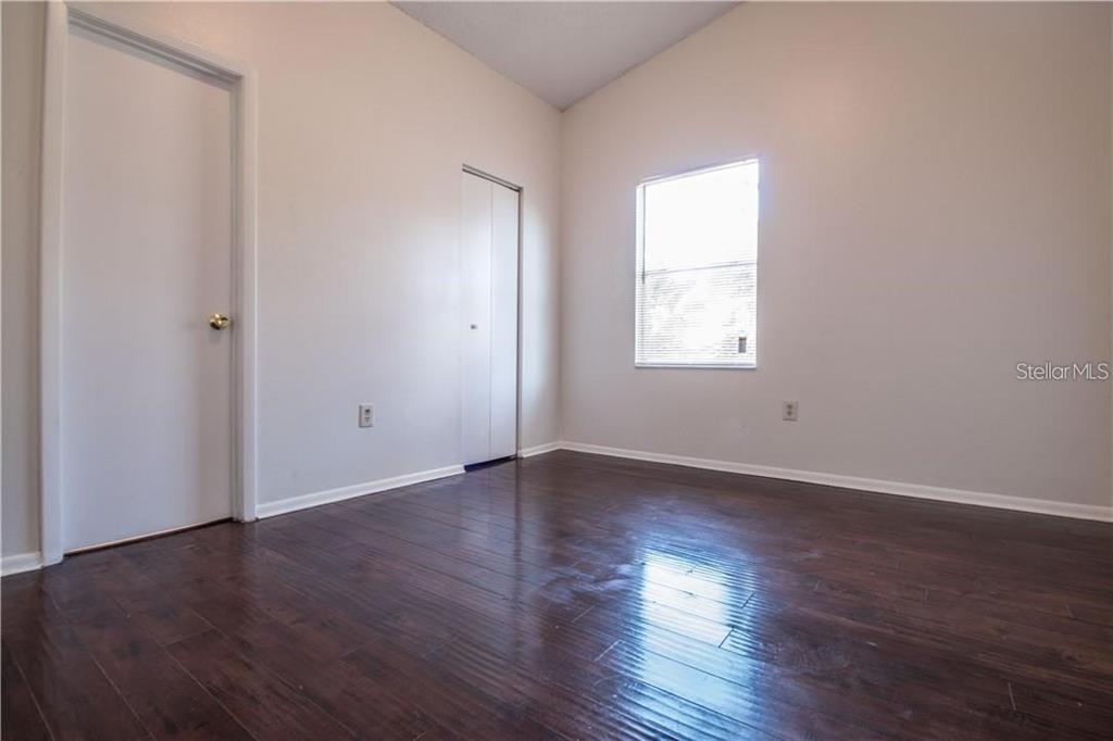 An empty bedroom with dark wood-look flooring, white walls, a window, and two doors — 1003 WINTERBERRY LANE, ORLANDO, FL