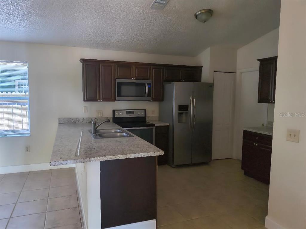 A kitchen features dark wood cabinets, stainless steel appliances, and a granite-look countertop island — 1003 WINTERBERRY LANE, ORLANDO, FL