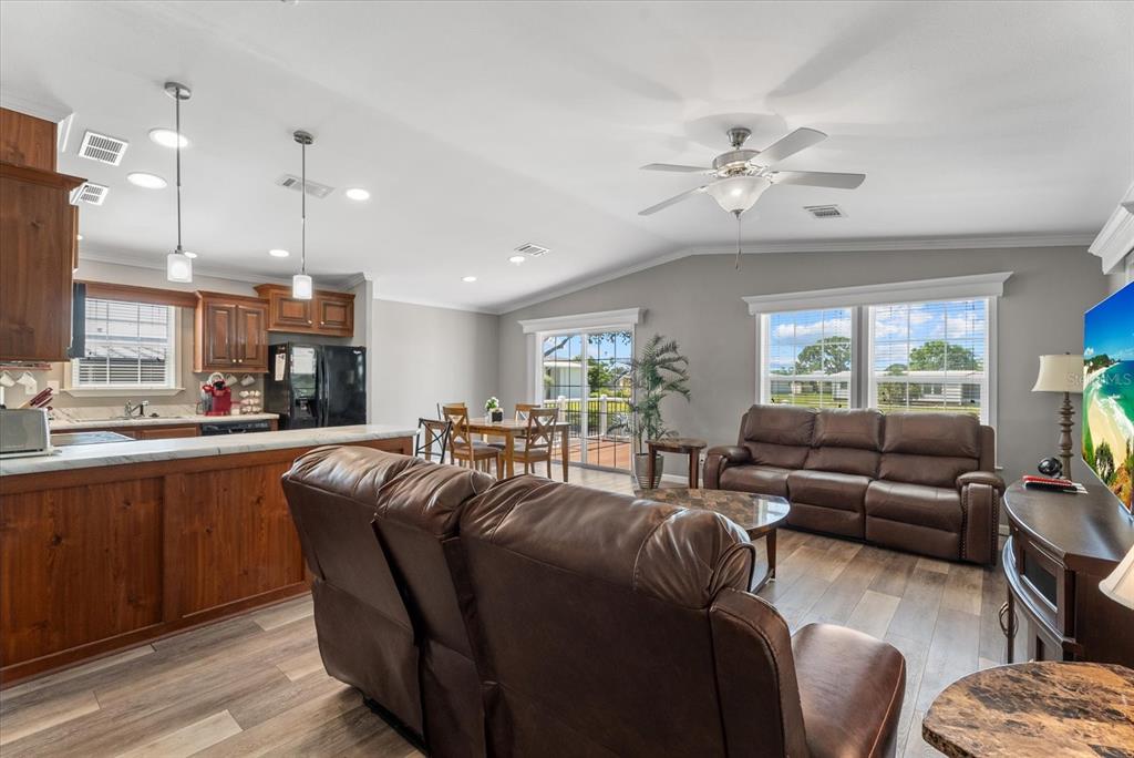 An open-concept living room and kitchen featuring wood cabinets, brown leather furniture, and sliding doors — 714 FAIRMOUNT DRIVE, NORTH PORT, FL