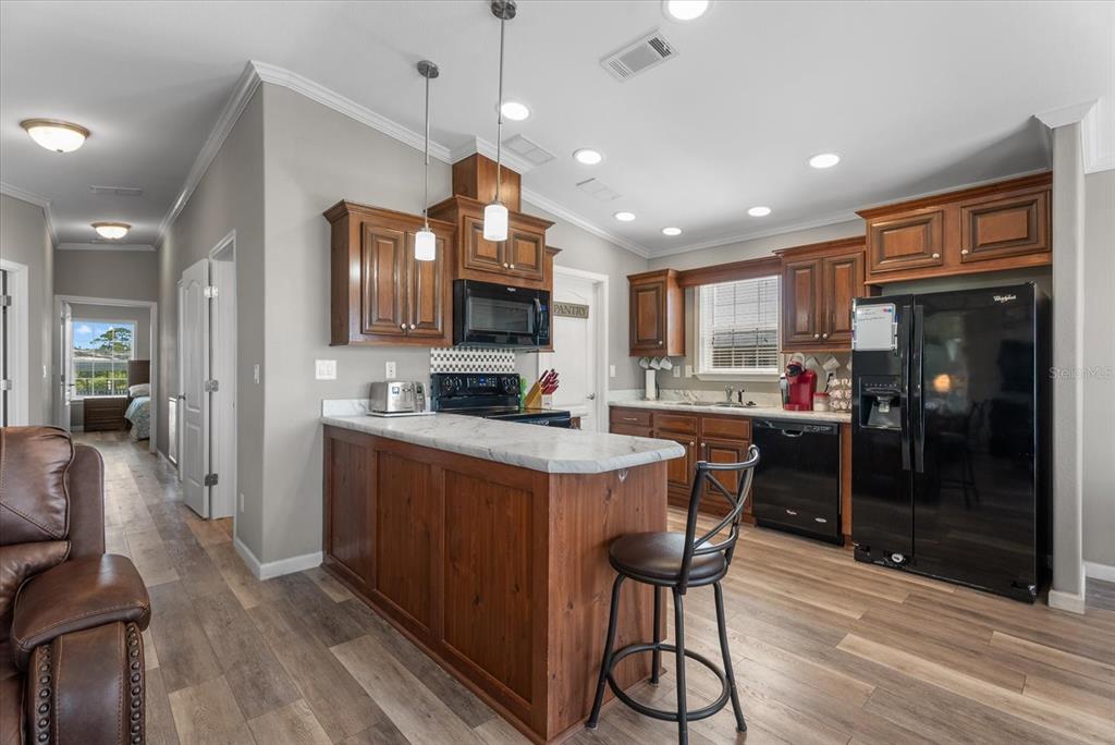A kitchen features wood cabinets, a marble-topped island, black appliances, and light wood-look flooring — 714 FAIRMOUNT DRIVE, NORTH PORT, FL