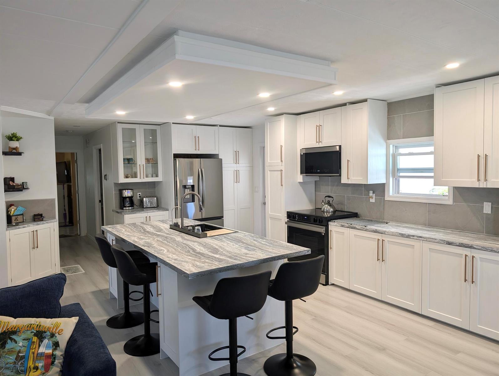 A modern kitchen features a large island with a stone countertop, white cabinets, and black stools — 37045 Exuma Bay, Boynton Beach FL 33436, BOYNTON BEACH, FL