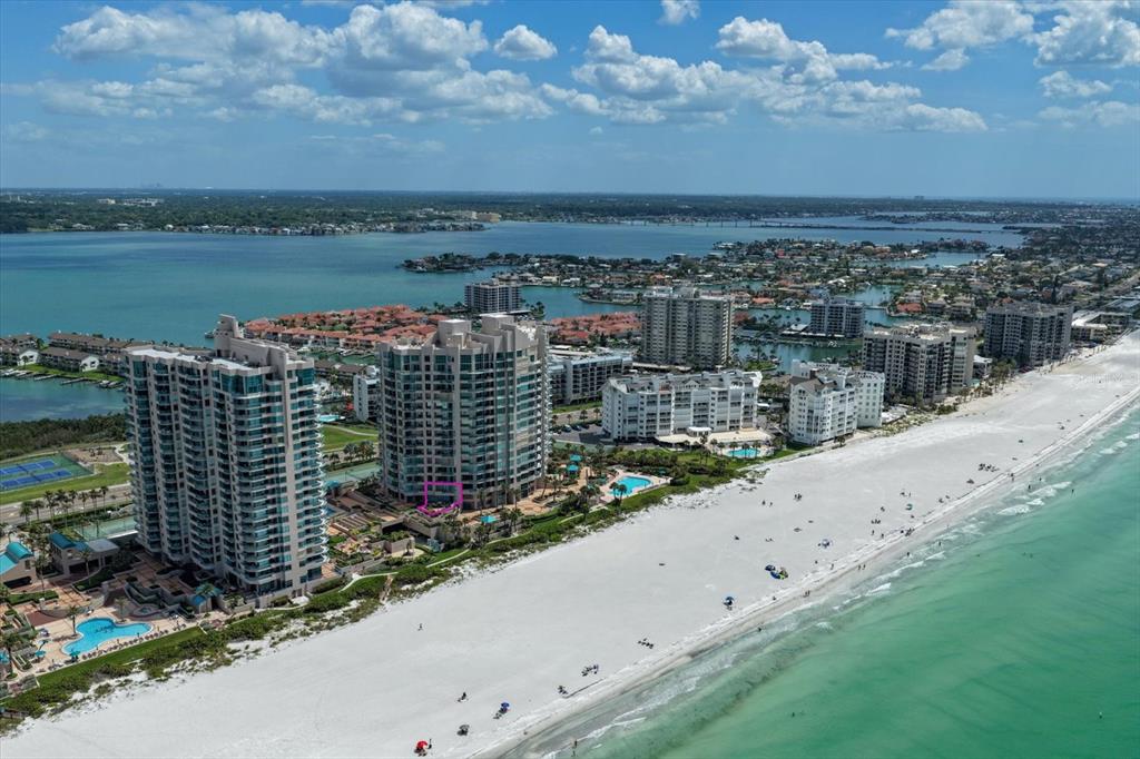 An aerial view shows high-rise beachfront condominiums along a white sand beach and turquoise water — 1560 GULF BOULEVARD UNIT 304, CLEARWATER, FL