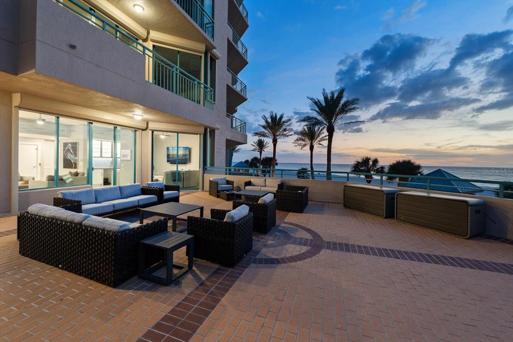 A large outdoor patio with wicker furniture overlooks the ocean at sunset — 1560 GULF BOULEVARD UNIT 304, CLEARWATER, FL