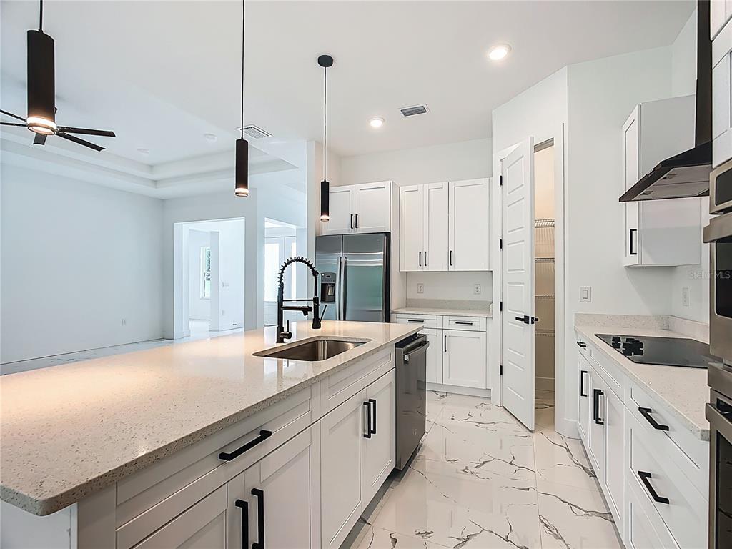 A modern kitchen features white cabinets, quartz countertops, a center island, and marble-look tile flooring — 2105 DORMAN ROCK PLACE, PLANT CITY, FL