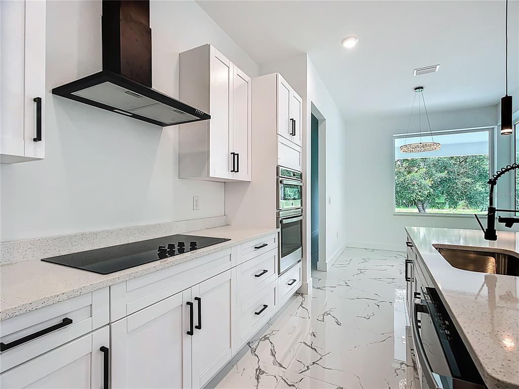 A modern kitchen features white cabinets, quartz countertops, stainless steel appliances, and marble-patterned tile flooring — 2105 DORMAN ROCK PLACE, PLANT CITY, FL