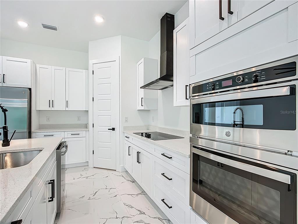 A modern kitchen features white cabinets, stainless steel appliances, quartz countertops, and marble-patterned tile flooring — 2105 DORMAN ROCK PLACE, PLANT CITY, FL
