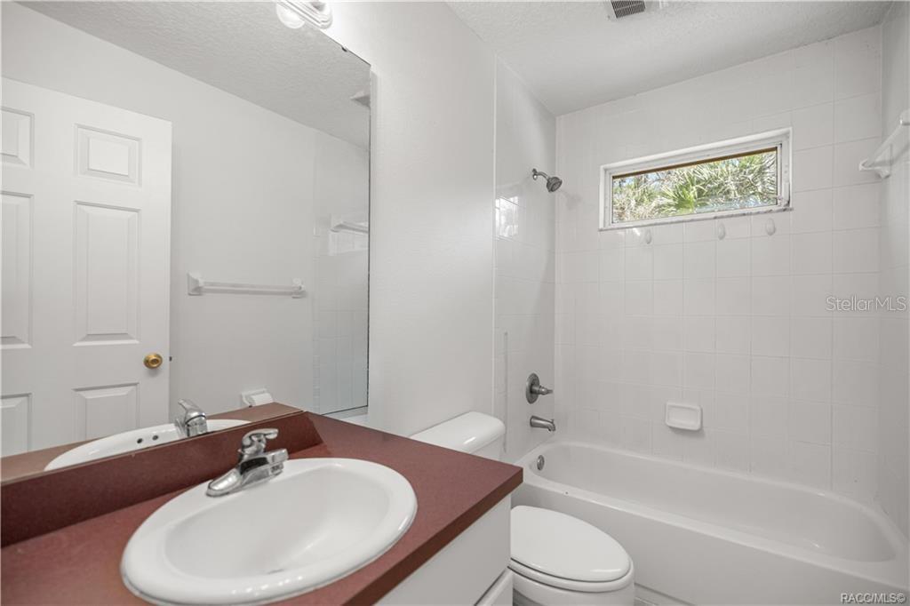 A bathroom features a white vanity with a red countertop, a toilet, and a tub-shower — 10 PATRICIA ROAD, YANKEETOWN, FL