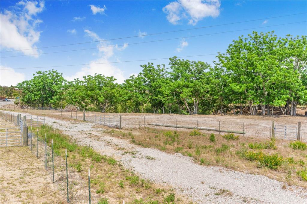 A gravel driveway leads through a fenced pasture toward a line of mature trees — LAKE HATCHINEHA ROAD, HAINES CITY, FL