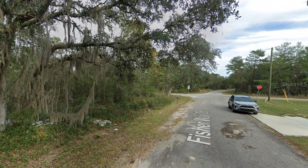 A paved road leads to an intersection near a wooded lot with Spanish moss trees — FISHER WAY DR LOT 16, OCKLAWAHA, FL