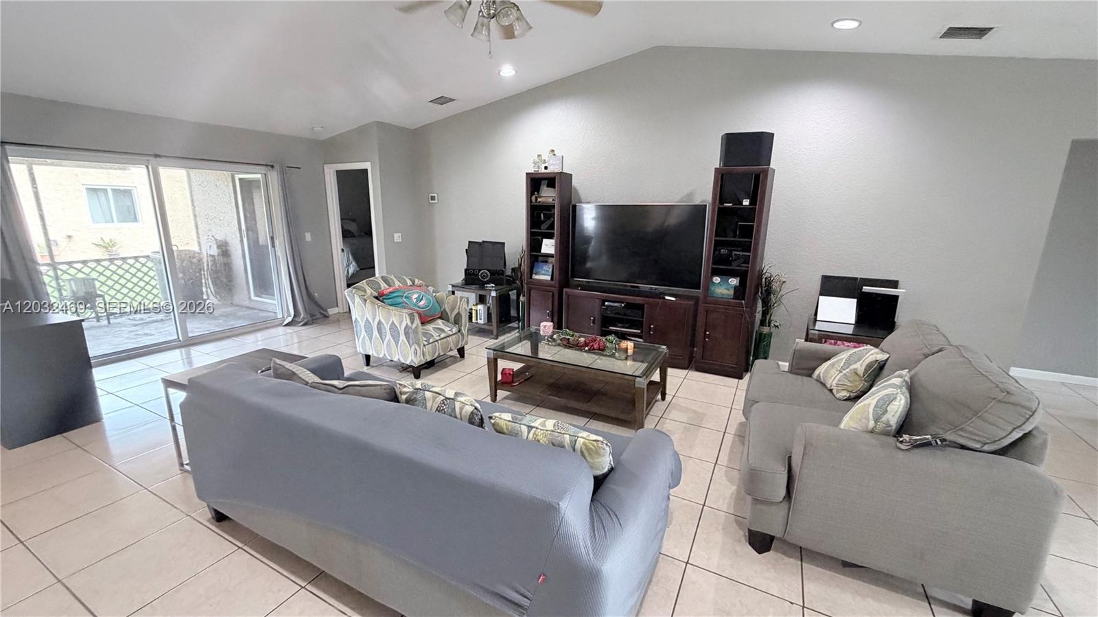 A living room features a vaulted ceiling, tile flooring, a television console, and gray furniture — 5356 NW 93rd Ter, Sunrise FL 33351, SUNRISE, FL