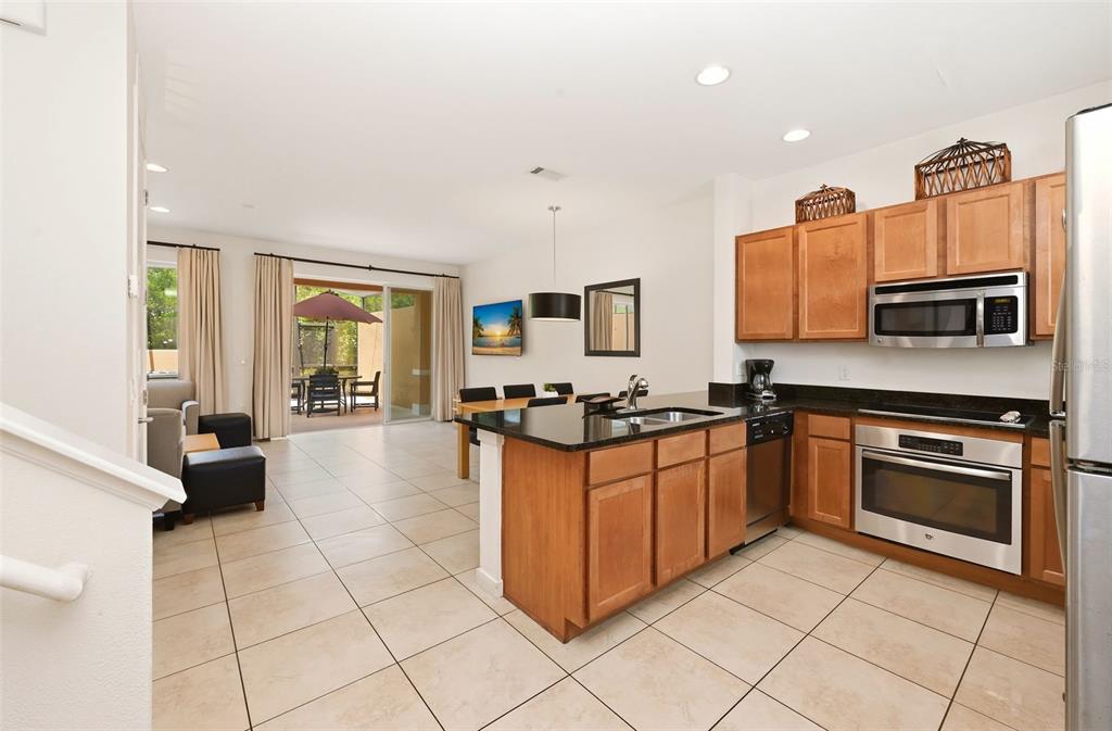 A kitchen with wood cabinets and granite countertops opens to a dining area and patio — 2606 ROADSTER LANE, KISSIMMEE, FL