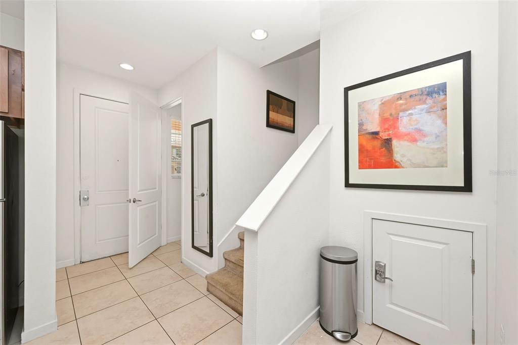 An entryway with tile flooring, a staircase, a framed painting, and a small storage door — 2606 ROADSTER LANE, KISSIMMEE, FL