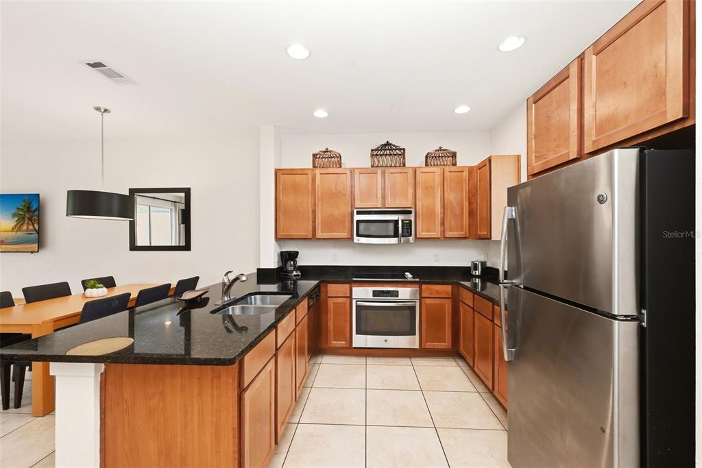 A kitchen with wood cabinets, black countertops, stainless steel appliances, and light tile flooring — 2606 ROADSTER LANE, KISSIMMEE, FL