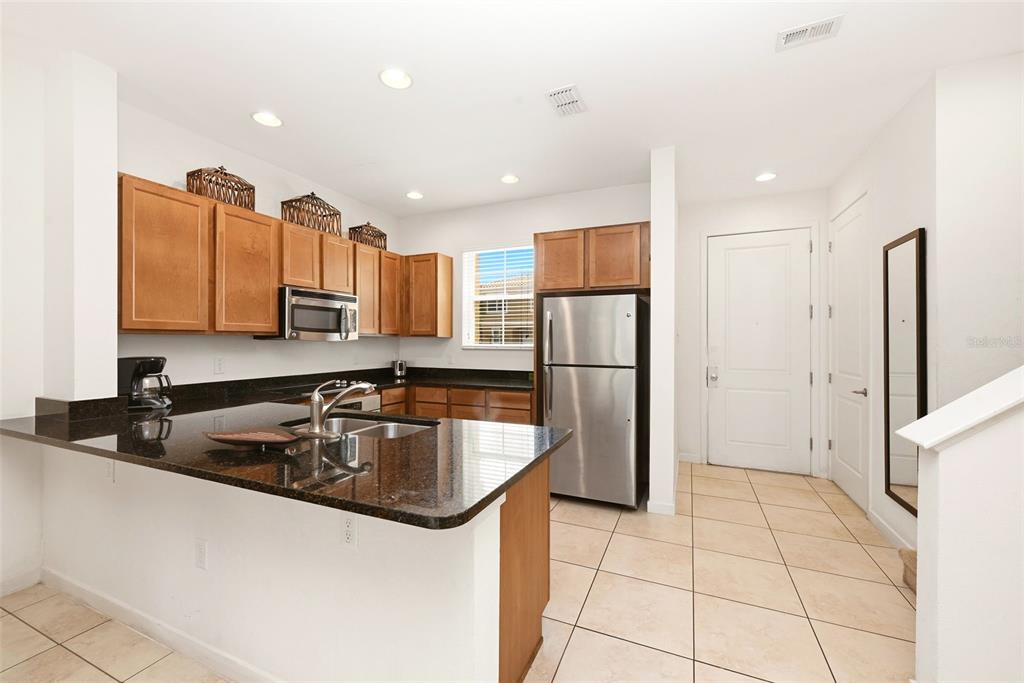 A kitchen features wood cabinets, dark granite countertops, stainless steel appliances, and tile flooring — 2606 ROADSTER LANE, KISSIMMEE, FL