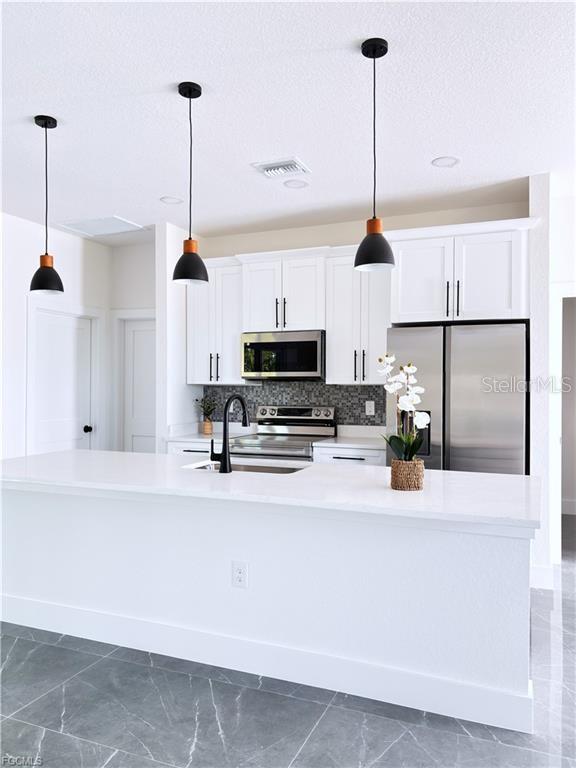 A modern kitchen features white cabinets, stainless steel appliances, and a large quartz island — 842 GIORGIO AVENUE S, LEHIGH ACRES, FL