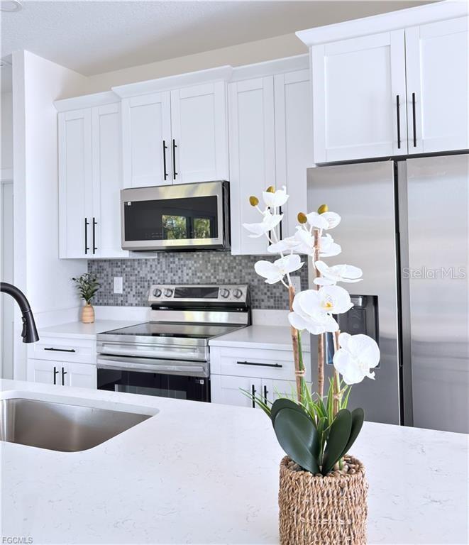 A modern kitchen features white cabinets, stainless steel appliances, and a quartz-topped island — 842 GIORGIO AVENUE S, LEHIGH ACRES, FL