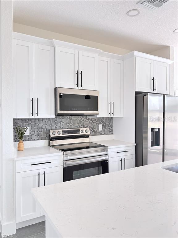 A kitchen features white cabinets, stainless steel appliances, a mosaic backsplash, and a quartz countertop — 842 GIORGIO AVENUE S, LEHIGH ACRES, FL
