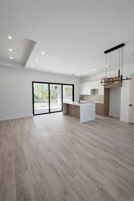 A modern open-concept kitchen and living area features light wood-look tile flooring and sliding doors — 1097 CORNELIUS BOULEVARD, PORT CHARLOTTE, FL