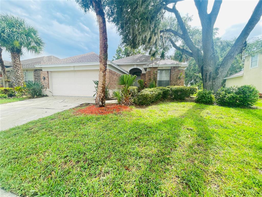 A single-story house with a two-car garage, brick facade, and a large oak tree — 1738 GOLFVIEW DRIVE, KISSIMMEE, FL