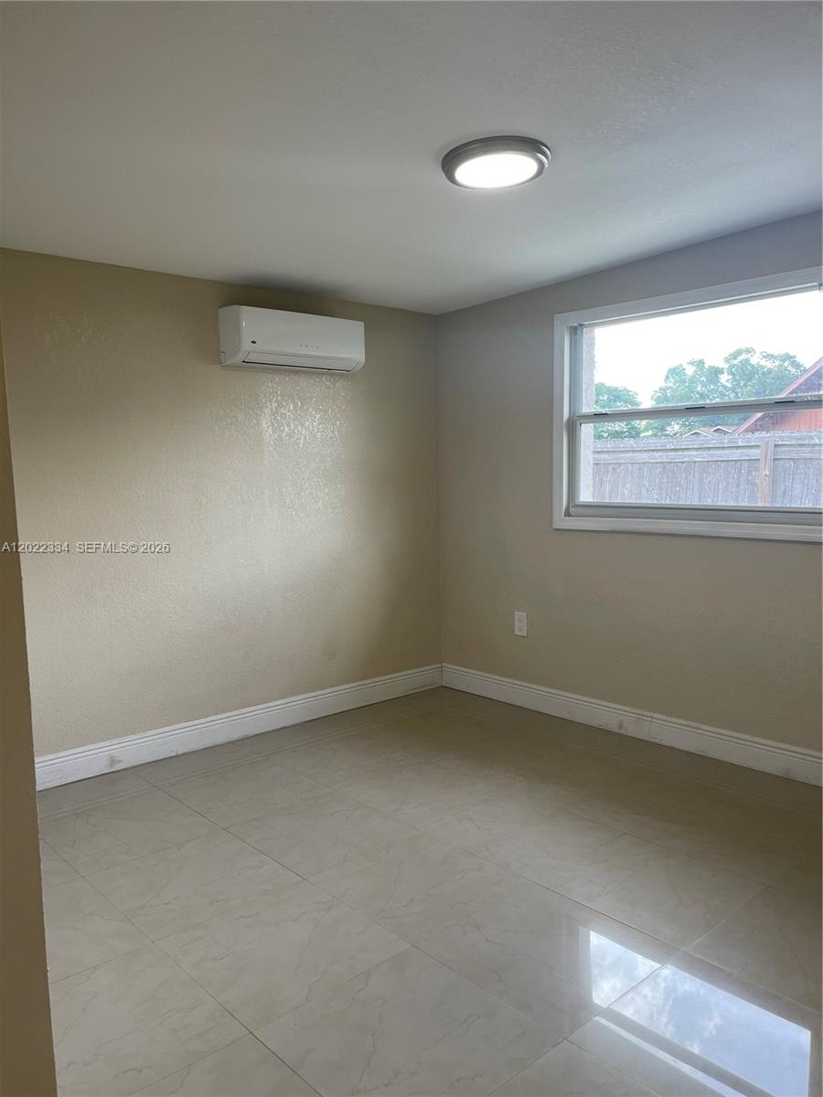 An empty room features beige walls, light-colored tile flooring, a window, and a wall-mounted air conditioner — 4617 Navarre Ave # B, Sebring FL 33872, SEBRING, FL