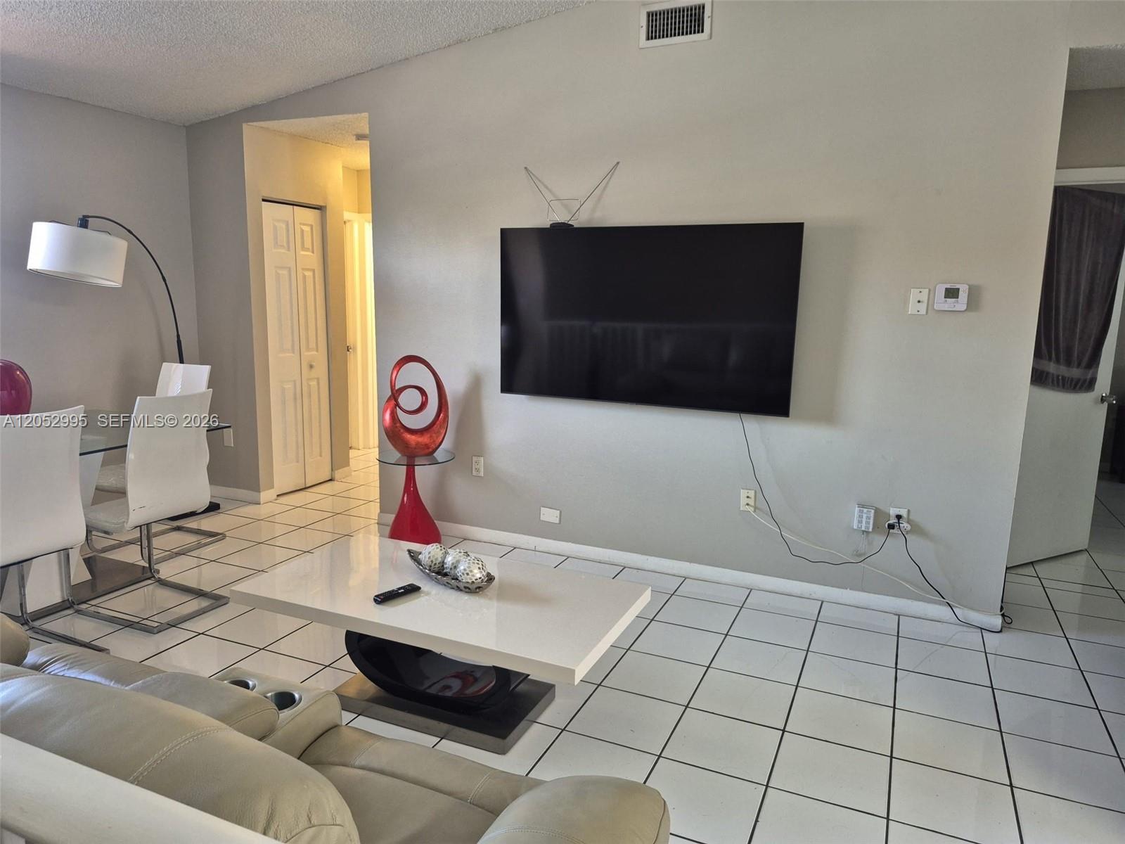 A living room features a wall-mounted television, a white coffee table, and tiled flooring — 7818 W 34th Ln # 201, Hialeah FL 33018, HIALEAH, FL