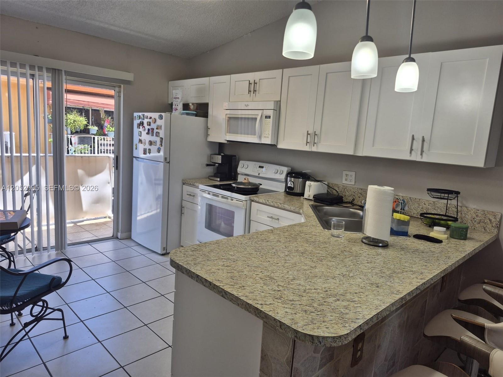 A kitchen features white cabinets, granite countertops, a white refrigerator, and a sliding glass door — 7818 W 34th Ln # 201, Hialeah FL 33018, HIALEAH, FL