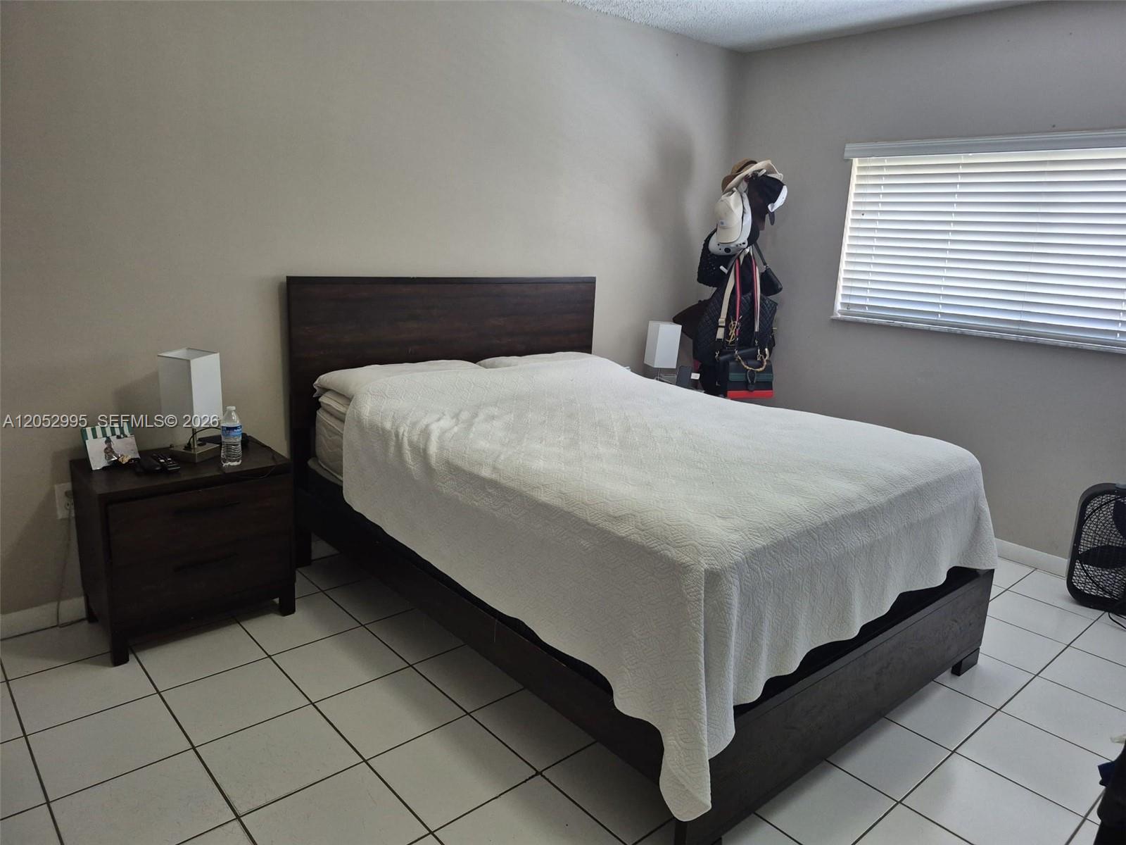 A bedroom features a dark wood bed frame, a matching nightstand, and white tile flooring — 7818 W 34th Ln # 201, Hialeah FL 33018, HIALEAH, FL