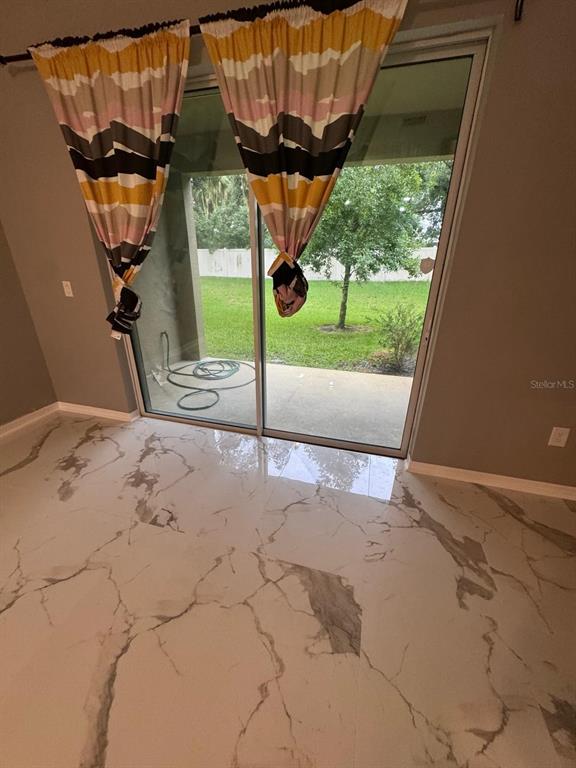 A room with white marble-patterned tile flooring features sliding glass doors leading to a backyard — 2121 BROADWAY VIEW AVENUE, BRANDON, FL