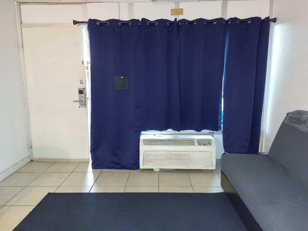 A room with tiled floors, a dark sofa, blue curtains, and a wall-mounted air conditioner — 43420 HIGHWAY 27 UNIT 157, DAVENPORT, FL