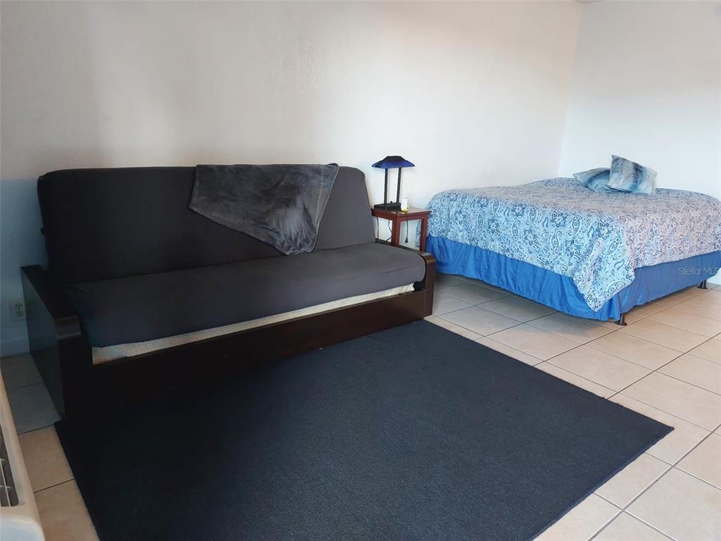 A room features a dark gray futon on a rug next to a bed — 43420 HIGHWAY 27 UNIT 157, DAVENPORT, FL