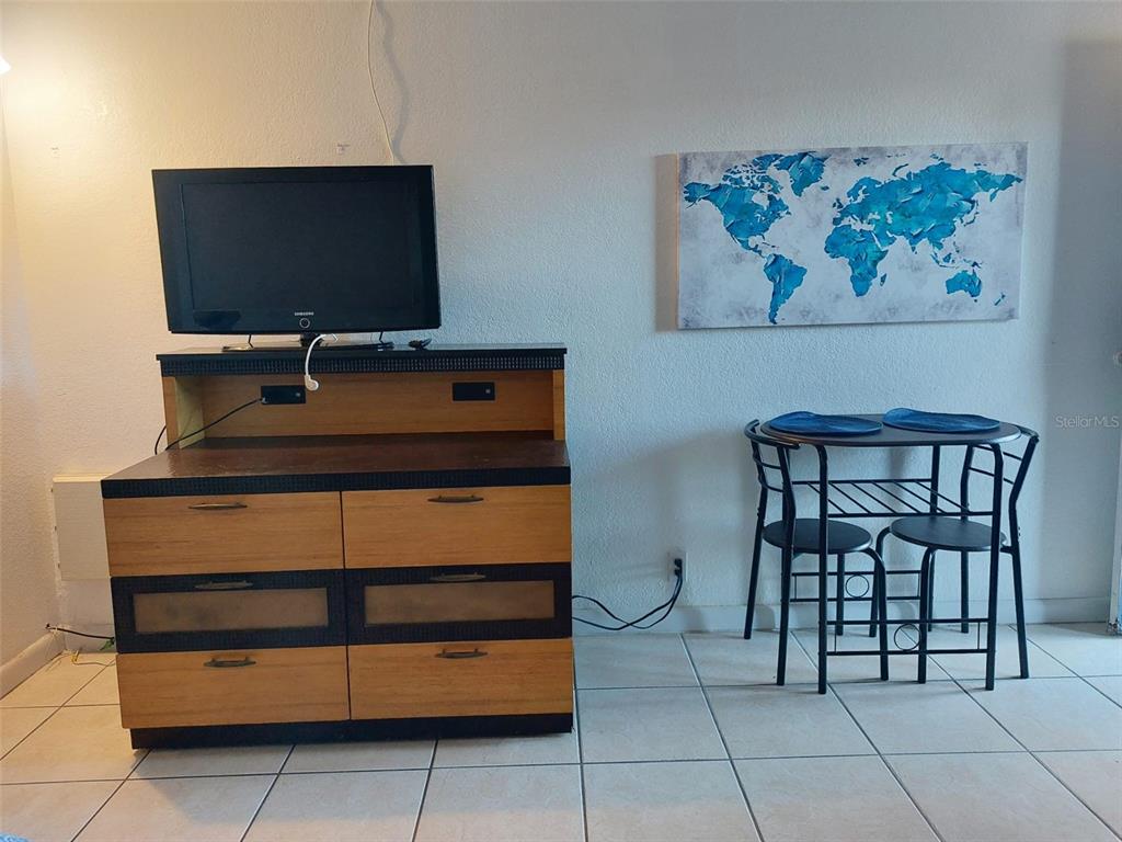 A room features a wooden dresser with a television and a small dining set nearby — 43420 HIGHWAY 27 UNIT 157, DAVENPORT, FL