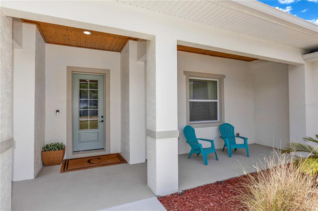 A covered front porch features a light blue door, two turquoise chairs, and wood-paneled ceilings — 1530 PERIWINKLE AVENUE, DELAND, FL