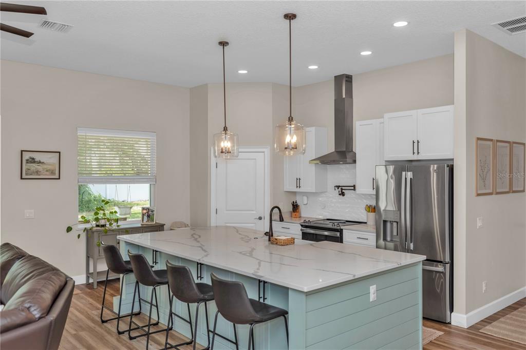 A kitchen features a large light blue island with quartz countertops and three bar stools — 1530 PERIWINKLE AVENUE, DELAND, FL