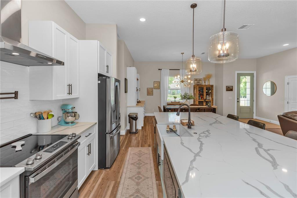 A modern kitchen features white cabinets, a marble-topped island, stainless steel appliances, and wood flooring — 1530 PERIWINKLE AVENUE, DELAND, FL