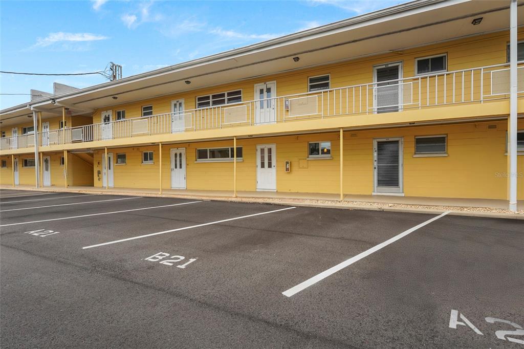 A two-story yellow apartment building features an exterior walkway and a paved parking lot — 2155 WOOD STREET UNIT A22, SARASOTA, FL