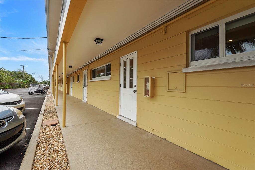 An exterior view of a yellow building with a covered walkway and multiple white doors — 2155 WOOD STREET UNIT A22, SARASOTA, FL