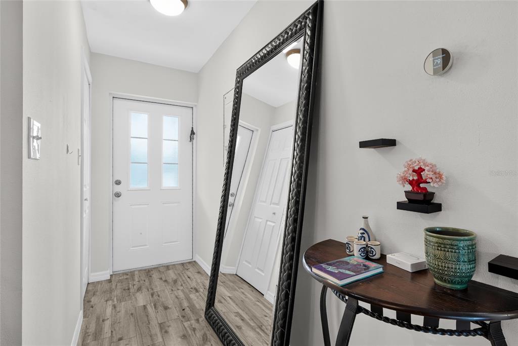 A bright entryway features wood-look flooring, a large floor mirror, and a small console table — 2155 WOOD STREET UNIT A22, SARASOTA, FL