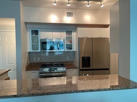 A kitchen features stainless steel appliances, granite countertops, and white cabinetry with glass-front accents — 625 Casa Loma Boulevard # 705, Boynton Beach FL 33435, BOYNTON BEACH, FL
