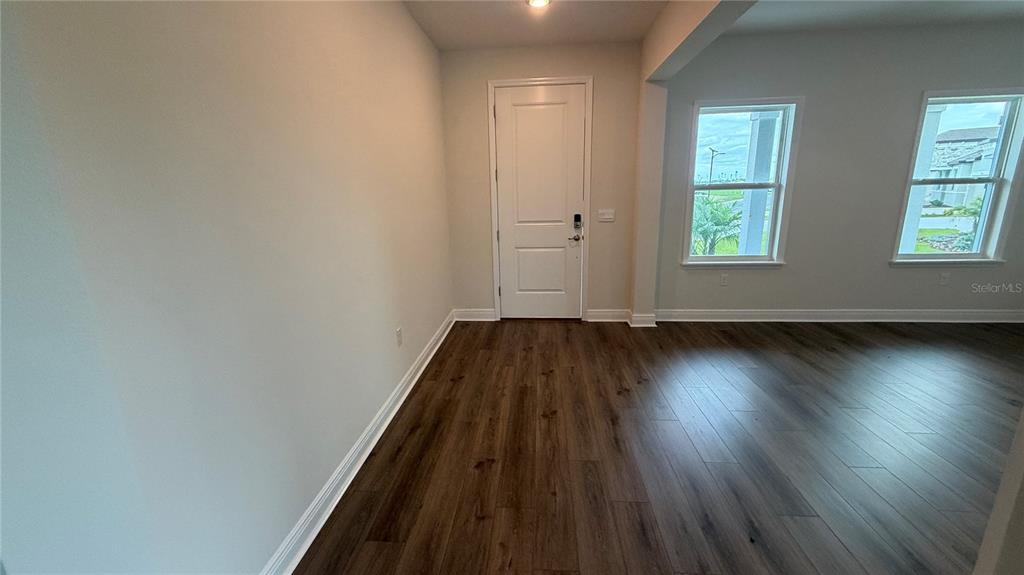 An empty room with wood-look flooring, a white entry door, and two windows — 4366 WINESAP WAY, LAKELAND, FL