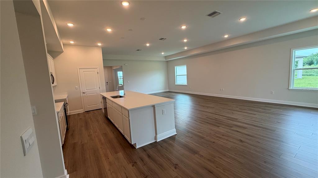 A kitchen with a white island and sink opens into a large, empty living area — 4366 WINESAP WAY, LAKELAND, FL