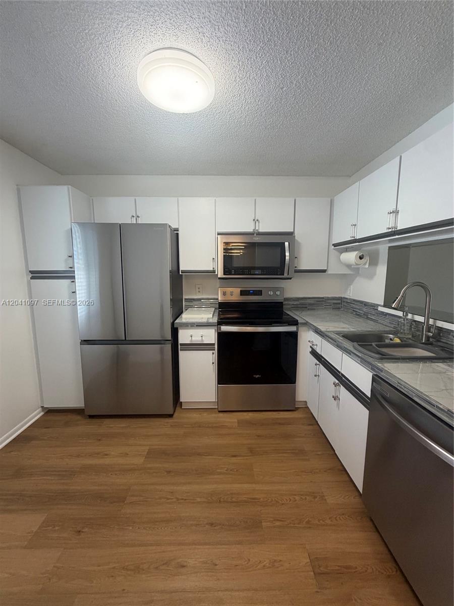 A kitchen features white cabinets, stainless steel appliances, and wood-look flooring — 3031 Holiday Springs Blvd # 7, Margate FL 33063, MARGATE, FL