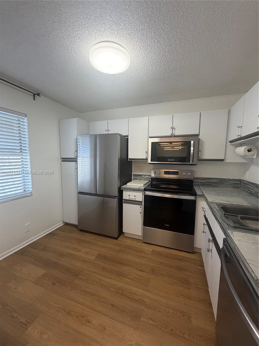 A kitchen features stainless steel appliances, white cabinetry, and wood-look flooring — 3031 Holiday Springs Blvd # 7, Margate FL 33063, MARGATE, FL