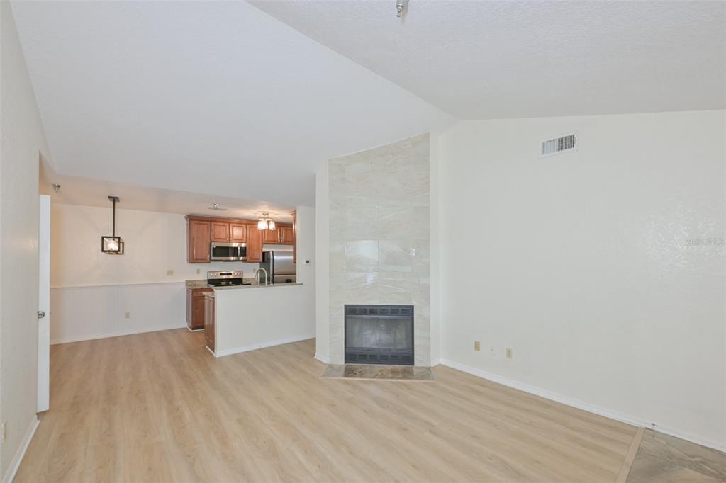 A living room with light wood flooring and a tiled fireplace connects to a kitchen — 10265 GANDY BOULEVARD N UNIT 1006, ST PETERSBURG, FL