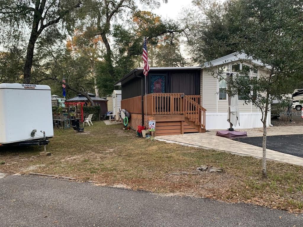 A mobile home features a wooden deck, a paved walkway, and a white utility trailer — 25247 NE 141ST LANE UNIT 248, FORT MC COY, FL