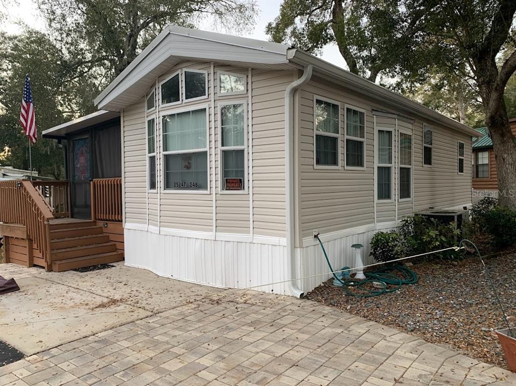 A beige mobile home with a wooden porch, American flag, and paver driveway — 25247 NE 141ST LANE UNIT 248, FORT MC COY, FL
